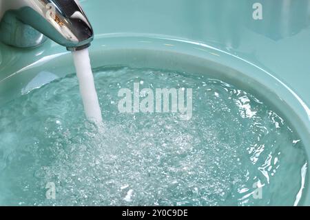 Fauceut gießt Wasser über ein grünes Glasbecken. Konzentrieren Sie sich auf den Wasserhahn Stockfoto