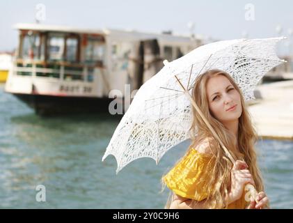 Junge glückliche Frau in gelbem Kleid, die einen Schirm auf dem Meeresboothintergrund hält Stockfoto