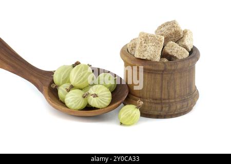 Stachelbeeren in einem Holzlöffel neben braunen Zuckerwürfeln in einer Holzschüssel, isoliert auf weißem Hintergrund, Beerenmarmelade, Kompottzubereitung Stockfoto