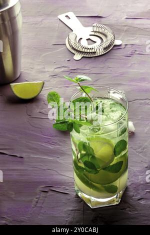 Mojito-Cocktail. Kaltes Sommergetränk mit Limette, frischer Minze und Eis. Kühles Getränk auf violettem Hintergrund, Lebensmittelfotografie Stockfoto