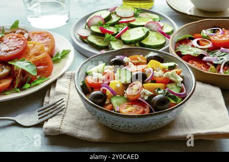 Frische vegetarische Salate, eine Auswahl. Auswahl an Tellern und Schüsseln mit grünem Gemüse. Gesunde Ernährung. Griechischer Salat, Tomaten, Gurken usw. Stockfoto