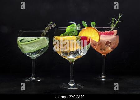 Ausgefallene Cocktails mit frischem Obst. Gin Tonic Drinks mit Eis auf einer Party, auf schwarzem Hintergrund. Alkohol mit Gurke, Orange, Rosmarin, Minze Stockfoto