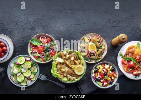 Frische Salate, Overhead Flat Lay Shot einer Auswahl. Auswahl an Tellern und Schüsseln mit grünem Gemüse. Gesundes Essen, Top-Shot auf einem schwarzen Schieferrücken Stockfoto