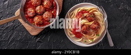 Panoramablick auf Fleischbällchen. Rindfleischbällchen, von oben in einer Pfanne geschossen und mit einem Teller Spaghetti-Pasta, auf schwarzem Schiefergrund Stockfoto