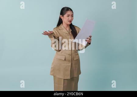 Schöne indonesische Regierungsangestellte in Khaki-Uniform, die einen Dokumentbericht mit einem verwirrten Ausdruck hält. PNS-Beamtenkonzept. Stockfoto