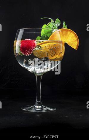 Schicker Cocktail mit frischem Obst. Gin Tonic Drink mit Eis auf einer Party, auf schwarzem Hintergrund. Alkohol mit Orange, Minze und Erdbeere Stockfoto