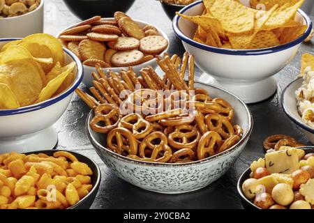 Salzige Snacks, Partymischung. Eine Auswahl knuspriger Vorspeisen in Schüsseln auf einem Tisch. Kartoffel- und Tortilla-Chips, Cracker, Popcorn usw. Stockfoto