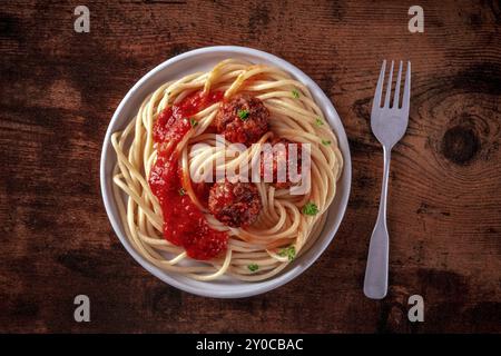 Fleischbällchen. Rindfleischbällchen, über dem Kopf flacher Lay Shot mit Spaghetti-Pasta, Petersilie und Tomatensauce, auf einem rustikalen hölzernen Hintergrund, Lebensmittelfotografie Stockfoto