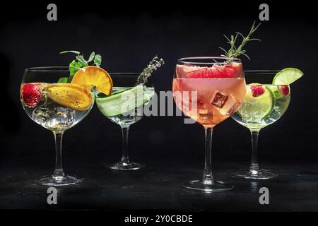 Ausgefallene Cocktails mit frischem Obst. Viele Gin Tonic Drinks mit Eis auf einer Party, auf schwarzem Hintergrund. Alkohol mit Kräutern und Blumen, Lebensmittelfoto Stockfoto