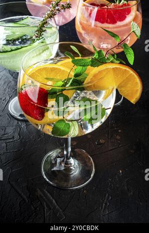 Ausgefallene Cocktails mit frischem Obst. Gin Tonic Drinks mit Eis auf einer Party, auf schwarzem Hintergrund. Alkohol mit Minze, Gurke, Zitrusfrüchten, ein Varié Stockfoto