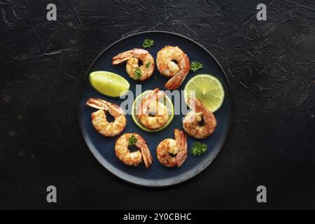 Shrimps, oben flach auf Schwarz geschossen. Gekochte Garnelen mit Limette auf blauem Teller, Gourmet-Vorspeise, Lebensmittelfotografie Stockfoto