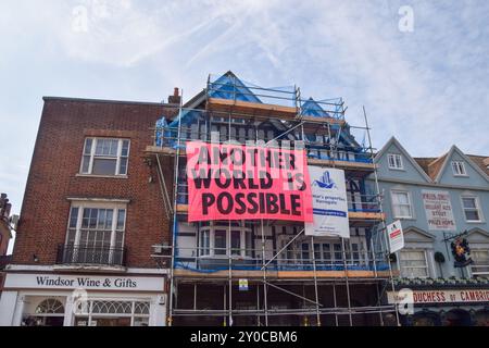 Windsor, Großbritannien. September 2024. Demonstranten hängen ein Banner an einem Gebäude gegenüber von Windsor Castle. Aktivisten der Extinction Rebellion marschierten am letzten Tag ihrer dreitägigen Übernahme von Windsor „Upgrade Democracy“ und forderten einen Systemwechsel und die Regierung auf, gegen die Klimakrise zu handeln. Quelle: Vuk Valcic/Alamy Live News Stockfoto