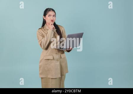 Durchdachte Regierungsangestellte in Khaki-Uniform, hält ihren Laptop und fragt sich über ihren Job. PNS-Beamtenkonzept. Stockfoto