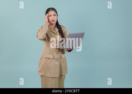 Verwirrte Regierungsangestellte, die ihren Laptop hält, sieht ernst aus, isoliert von blauem Hintergrund. PNS-Beamtenkonzept. Stockfoto