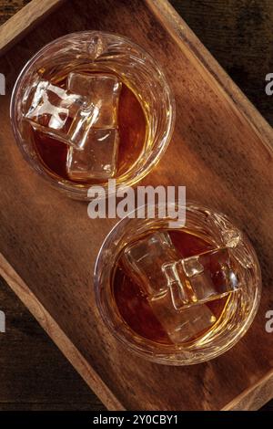 Whiskey in Gläsern mit Eis. Bourbon Whisky auf Felsen auf dunklem rustikalem Holzhintergrund, von oben aufgenommen Stockfoto