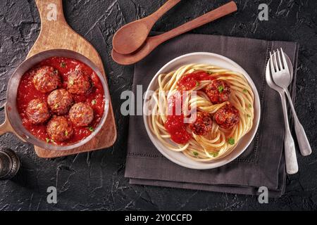 Fleischbällchen. Rindfleischbällchen, flach über dem Kopf liegend, in einer Pfanne und mit einem Teller Spaghetti-Pasta auf schwarzem Hintergrund Stockfoto