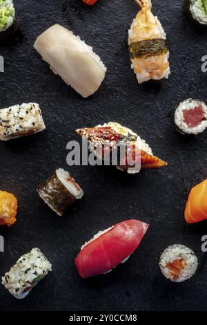 Sushi-Sorte, von oben geschossen. Brötchen, Maki, Nigiri auf schwarzem Schiefergrund, japanisches Essen. Aal, Garnelen, Thunfisch, Lachs, Felchen mit Reis, Essen Stockfoto