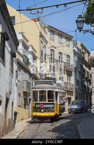 Die gelbe Straßenbahn fährt durch enge Gassen mit historischen Gebäuden unter blauem Himmel, Straßenbahnlinie 28, Carros Electricos de Lisboa, Electricos de Lisboa, ol Stockfoto