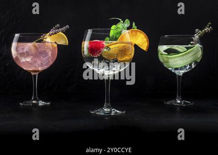 Ausgefallene Cocktails mit frischem Obst. Gin Tonic Drinks mit Eis auf einer Party, auf schwarzem Hintergrund. Alkohol mit Zitrone, Lavendel, Orange, Minze, Gurke Stockfoto