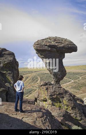 Eine junge Frau steht auf einem Felsvorsprung und blickt auf den berühmten Balanced Rock bei Buhl, Idaho Stockfoto