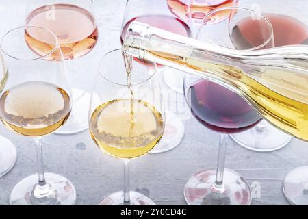 Bei einer Verkostung wird Weißwein in ein Glas gegossen. Rosen-, Rot- und Weißwein, Drinks auf einem Tisch in einem Weingut. Eine Auswahl an Weinen in vielen verschiedenen Farben, Stockfoto