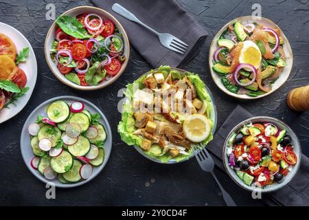 Frische Salate, Overhead Flat Lay Shot einer Auswahl. Auswahl an Tellern und Schüsseln mit grünem Gemüse. Gesundes Essen, Top-Shot auf einem schwarzen Schieferrücken Stockfoto