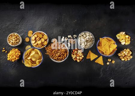 Salzige Snacks, Partymischung. Eine Auswahl knuspriger Vorspeisen, die von oben auf schwarzem Hintergrund mit Kopierbereich aufgenommen wurden. Kartoffeln und Tortilla-Chips, Cracker Stockfoto