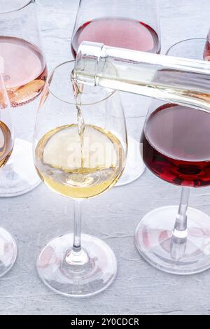 Wein in ein Glas bei einer Verkostung gießen. Rosen-, Rot- und Weißwein, Drinks auf einem Tisch in einem Weingut. Eine Auswahl an Weinen in verschiedenen Farben und Farbtönen, Stockfoto