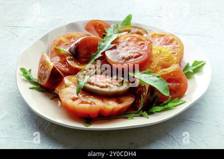 Frische Tomaten und Rucolasalat. Eine Vielzahl von Tomaten verschiedener Art mit Rucolablättern. Gesundes Sommeressen, Lebensmittelfotografie, Lebensmittelfotografie Stockfoto