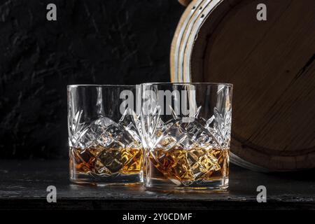 Whiskey in Gläsern mit Fass. Bourbon Whisky und ein Fass auf dunklem Hintergrund, eine Verkostung in einer Destillerie, Lebensmittelfotografie, Lebensmittelfotografie Stockfoto