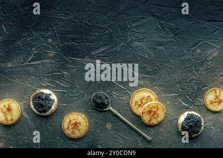Blinis mit schwarzem Kaviar und Frischkäse, oben auf schwarzem Steinhintergrund, Mini-Pfannkuchen, mit Kopierraum, Lebensmittelfotografie Stockfoto