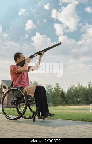 Außenporträt eines älteren Mannes, der einen Rollstuhl benutzt und ein Gewehr zum Himmel hält und auf ein fliegendes Ziel wartet Stockfoto