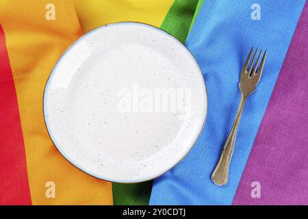 Gay Dinner Konzept. Ein Platz an einem Restauranttisch mit einem Teller und einer Gabel, ein flacher Lay-Shot über der LGBT-Regenbogenfahne, Lebensmittelfotografie, Stockfoto