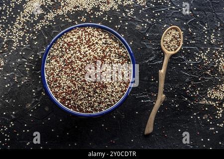 Quinoa-Mischung. Gemischte weiße, rote und schwarze Quinoa-Samen in einer Schüssel, oben flach auf schwarzem Hintergrund, mit einem Holzlöffel, Lebensmittelfotografie, Fo Stockfoto