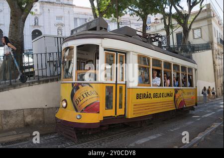 Eine gelbe Straßenbahn mit Beirao-Werbung fährt durch eine enge Stadtstraße, Leute an Bord, Straßenbahn, Linie 28, Carros Electricos de Lisboa, Electricos de Li Stockfoto