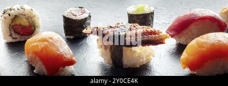 Sushi auf einem schwarzen Schieferplatten-Panorama. Nigiri mit Aal, Lachs und Thunfisch, Rolle mit Avocado und Maki mit Gurke auf schwarzem Hintergrund, Food Photogra Stockfoto