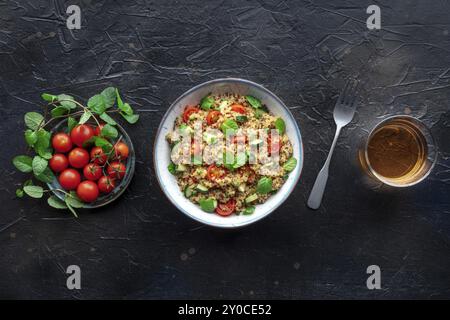 Quinoa Tabbouleh Salat in einer Schüssel, ein gesundes Abendessen mit Tomaten und Minze, über dem Kopf flacher Lay Shot mit einer Gabel und einem Getränk, auf schwarzem Stein Hintergrund Stockfoto