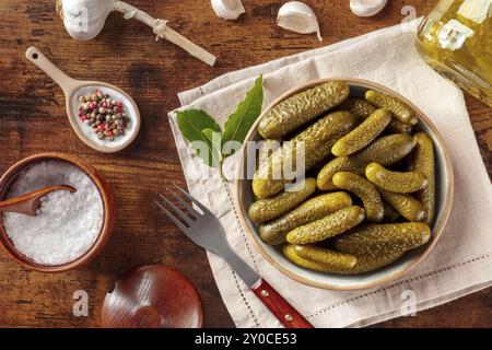 Eingelegte Gurken mit Salz, Pfeffer, Knoblauch und Lorbeerblatt. Fermentierte Lebensmittel. Hausgemachte Gurken in Dosen. Über dem Kopf flacher Lay-Shot auf einem rustikalen hölzernen Hintergras Stockfoto