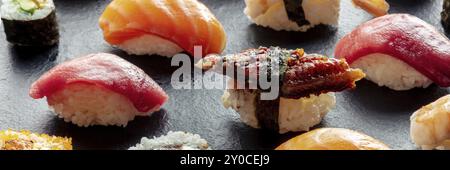 Sushi-Panorama. Nigiri mit Aal, Thunfisch, Lachs auf schwarzem Hintergrund, japanisches Essen auf einem Teller in einem asiatischen Restaurant, Lebensmittelfotografie, Lebensmittelfoto Stockfoto