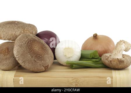 Shiitake-Pilze und verschiedene Zwiebeln auf einem Holzschneidebrett isoliert auf weißem Hintergrund. Rezepte und Heilkräuter Stockfoto