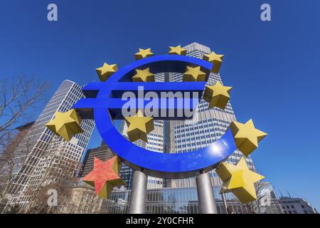 Eine große Euro-Symbolskulptur mit gelben Sternen vor modernen Wolkenkratzern an einem klaren blauen Himmel im Frankfurter Finanzviertel European CEN Stockfoto