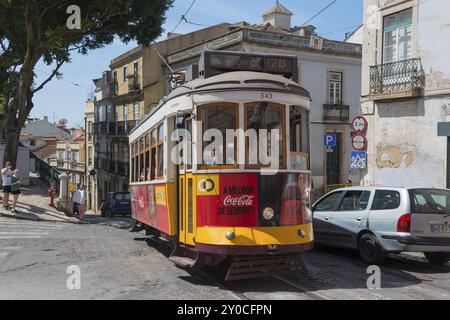 Eine gelbe und rote Straßenbahn fährt durch eine historische Stadtstraße, die von alten Gebäuden umgeben ist, Straßenbahnlinie 28, Carros Electricos de Lisboa, Electricos de Lisbo Stockfoto