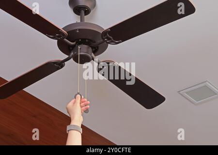 Deckenventilator aus Holz. Frau schaltet ein modernes Gerät ein, um den Raum mit Geschwindigkeitsregelung zu kühlen. Sommer und Wärme im Zimmer. Stockfoto