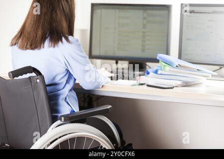 Ungültige oder behinderte junge geschäftsfrau sitzende Person Rollstuhl arbeiten Büro Schreibtisch computer Stockfoto