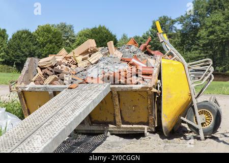 Metallbehälter gefüllt mit Schutt und Schubkarre außerhalb Stockfoto