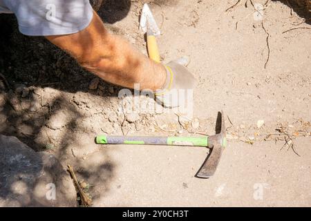 Arm eines Archäologen in einer archäologischen Grabung auf der Seite des Bodens befinden sich zwei Werkzeuge, eine kleine Spitzhacke und eine Kelle. Stockfoto