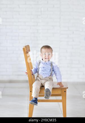 Schöne liebenswert lachendes Baby junge sitzen auf dem Stuhl. Lächelnde blauäugiges Kind sitzt auf einem Stuhl Stockfoto