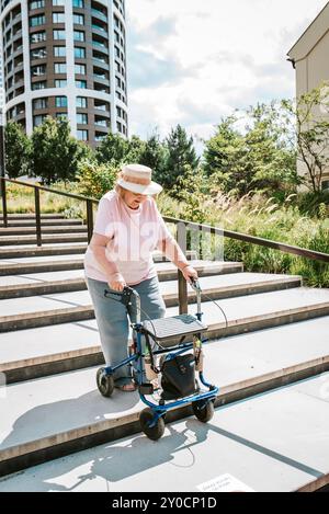 Eine ältere Frau, die mit Rollator die Treppe hinunter läuft und Besorgungen macht. Stockfoto