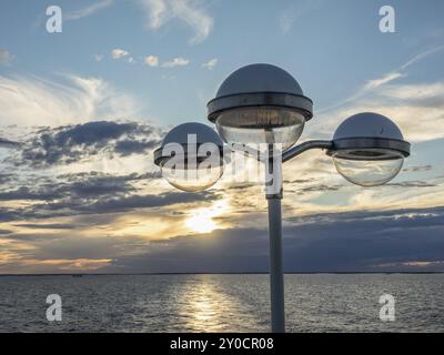 Eine Straßenlaterne vor einem stimmungsvollen Sonnenuntergang am Meer, der Himmel ist mit Wolken bedeckt und bietet eine romantische Atmosphäre, svaneke, bornholm, ostsee Stockfoto