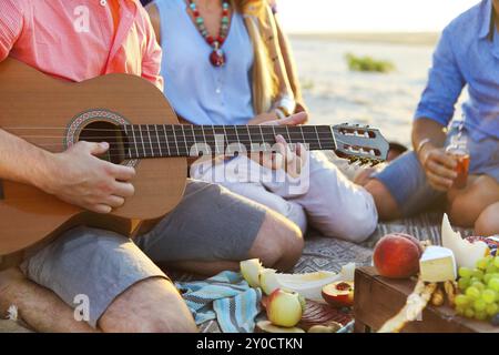 Freunde auf dem Sand am Strand im Kreis sitzen. Ein Mann spielt Gitarre. Nahaufnahme Stockfoto